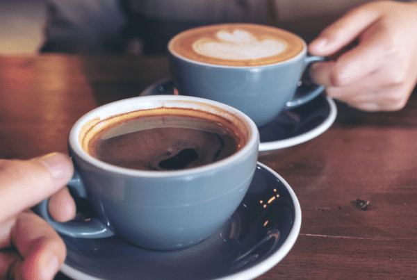 A cup of coffee with froth on a farmhouse kitchen table, symbolizing hospitality and meaningful conversations.