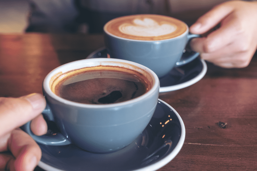 A cup of coffee with froth on a farmhouse kitchen table, symbolizing hospitality and meaningful conversations.