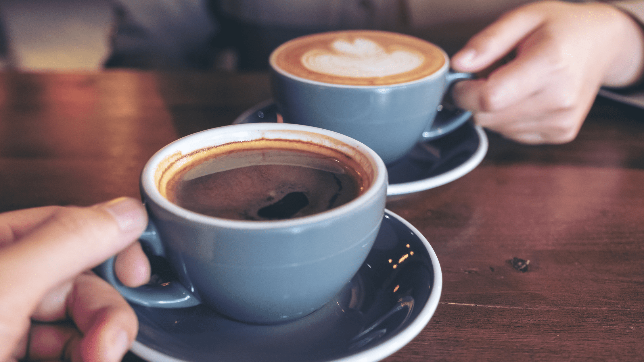 A cup of coffee with froth on a farmhouse kitchen table, symbolizing hospitality and meaningful conversations.